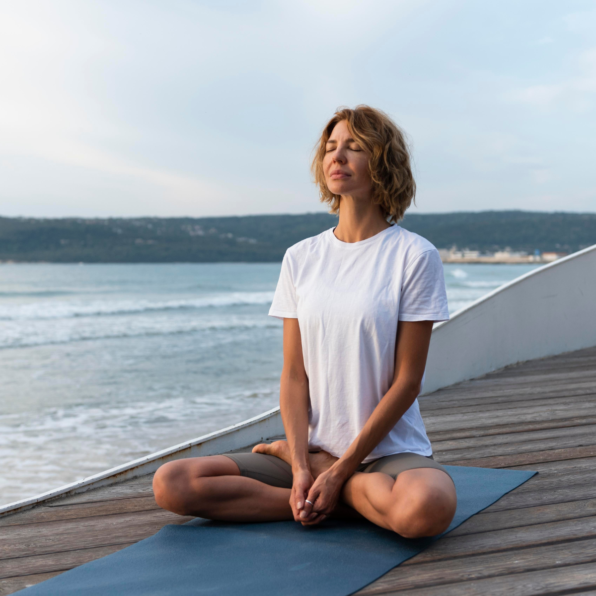 Woman practicing yoga on a mat by the ocean