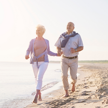 Two elderly people walking hand in hand on a beach.
