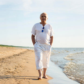 Person in white clothing standing on a beach with ocean waves.